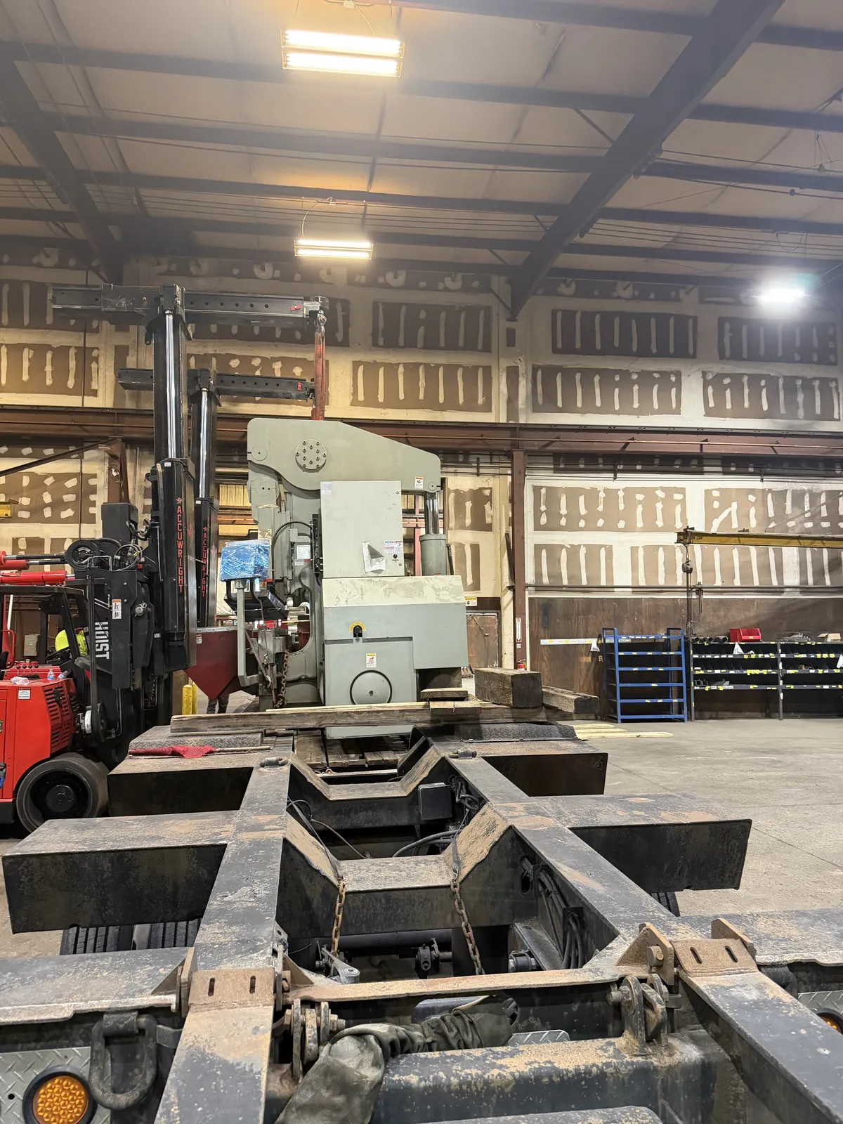 An Accuwright heavy forklift moving a large machine beside a lowboy trailer in an older plant
