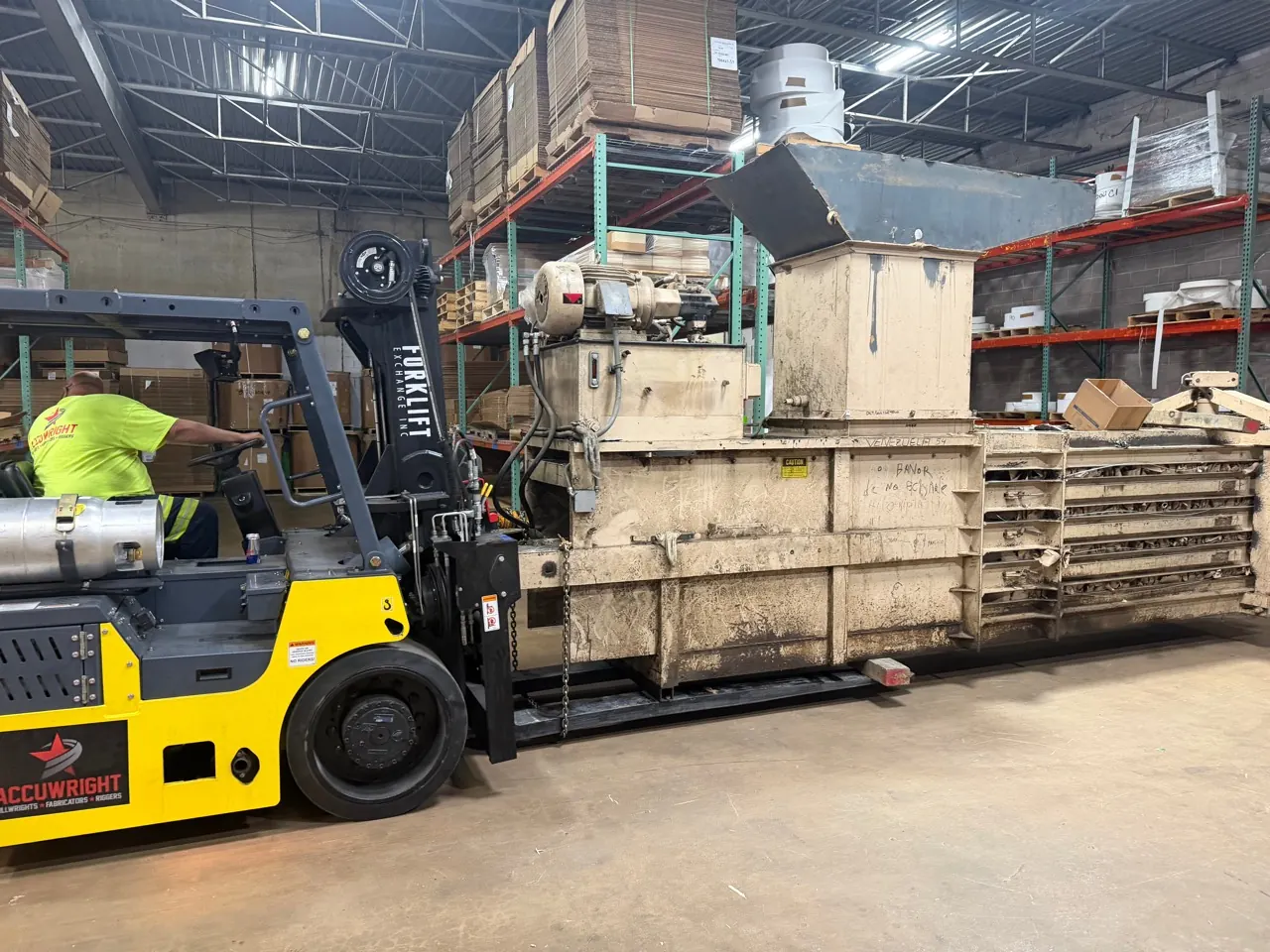 A yellow heavy forklift moving a large machine through a warehouse