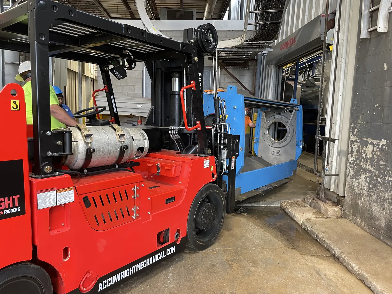 A branded Accuwright heavy forklift moving a large blue machine section through a tight plant doorway