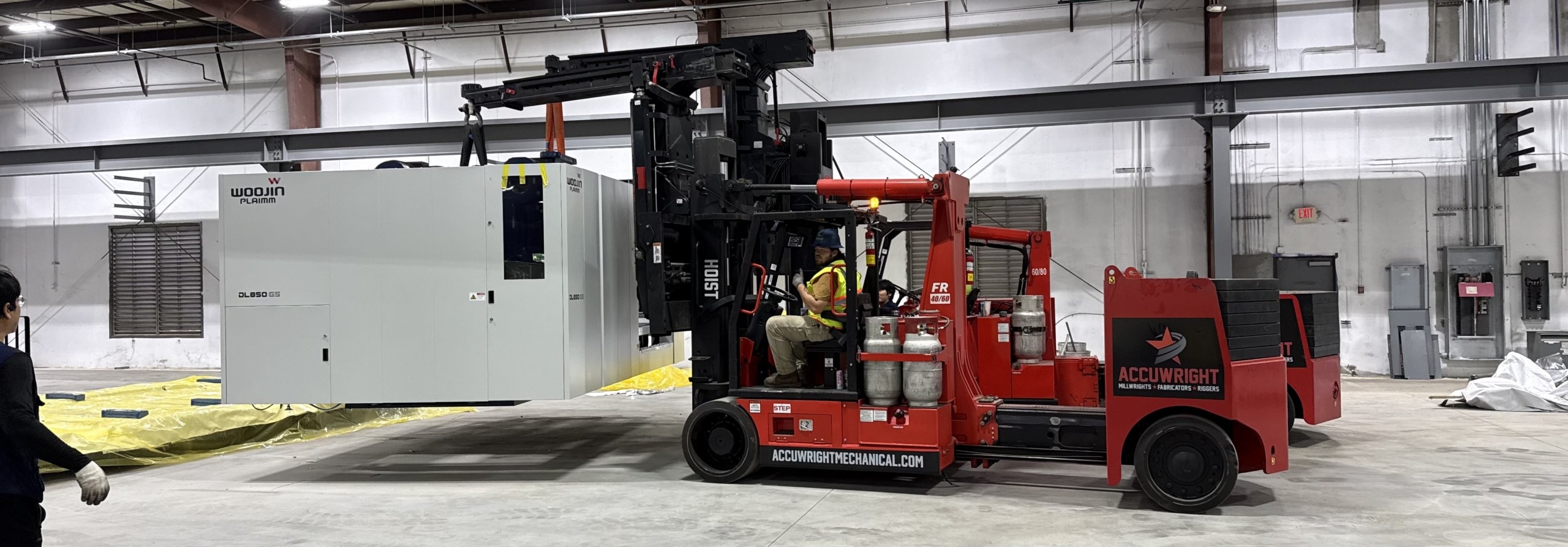 Accuwright Mechanical crew setting a Woojin Plaimm DL850 GS injection moulding machine with a Hoist FR 40/60 forklift inside a plant