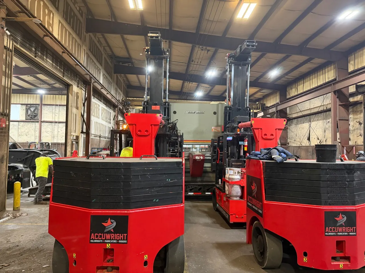 Two Accuwright heavy forklifts working in tandem to position an Accurpress machine inside a plant