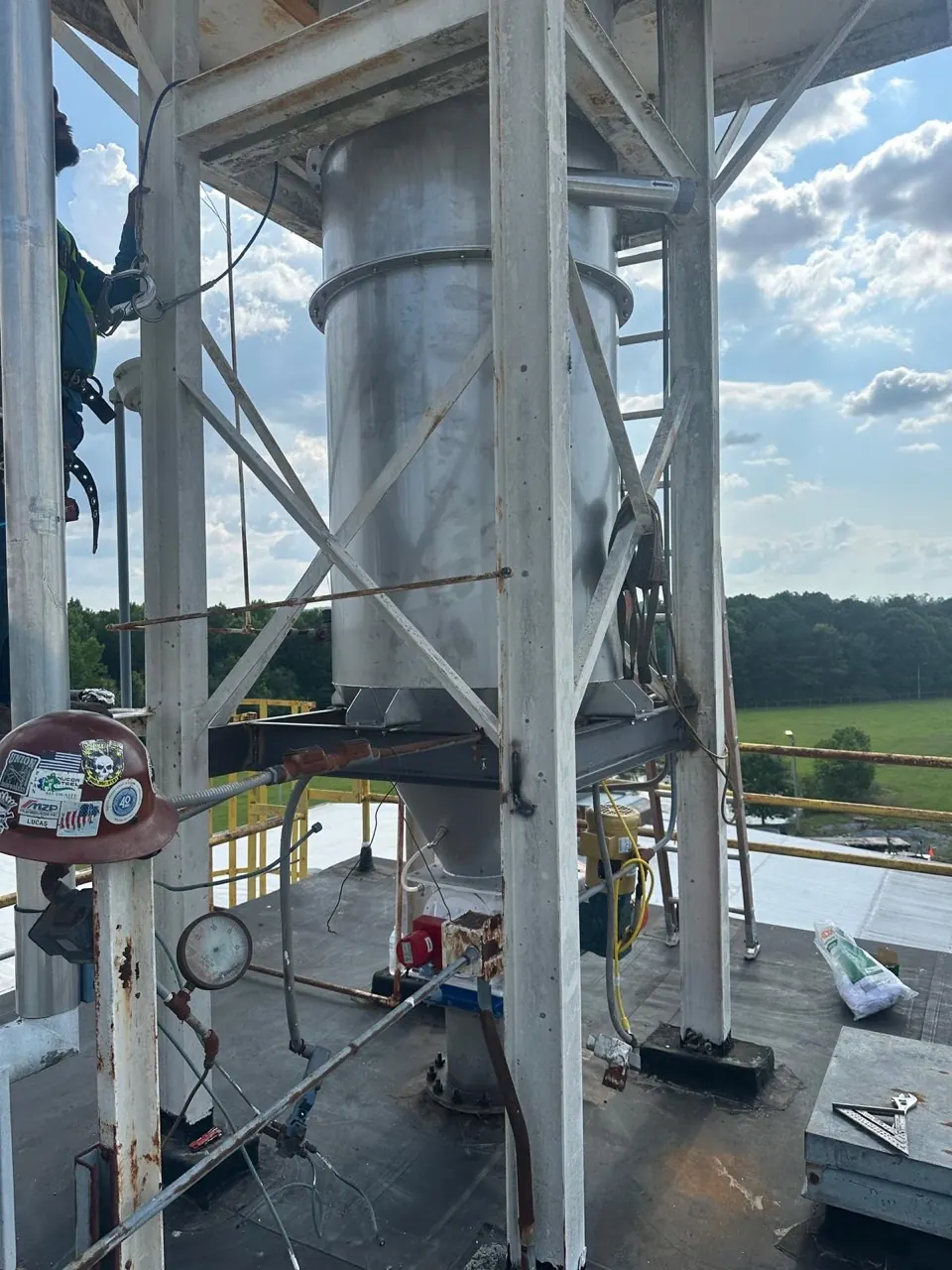 A harnessed Accuwright craft worker at elevation beside a stainless process vessel