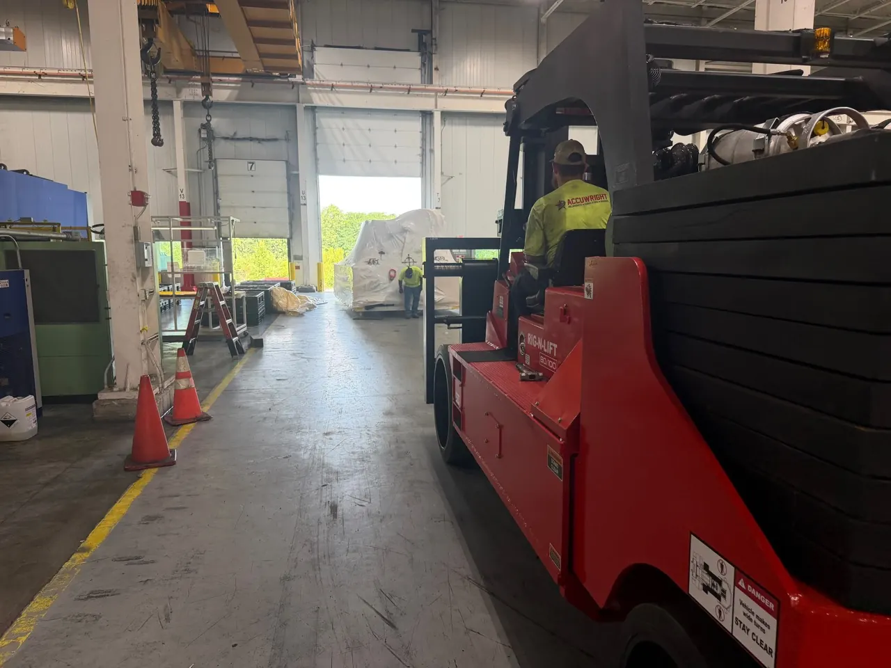 A branded red Accuwright machinery mover taking a wrapped machine toward a plant opening