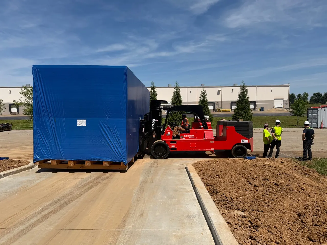 An Accuwright heavy forklift carrying a large wrapped industrial crate across an outdoor yard