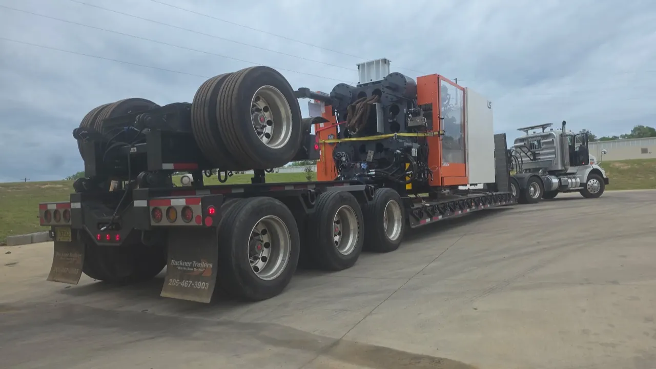 A tractor and lowboy trailer hauling a large industrial machine press down the road
