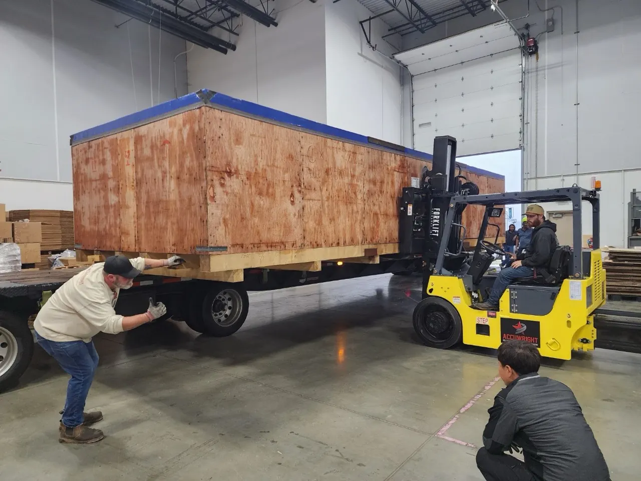 An Accuwright forklift loading a long wooden crate onto a trailer