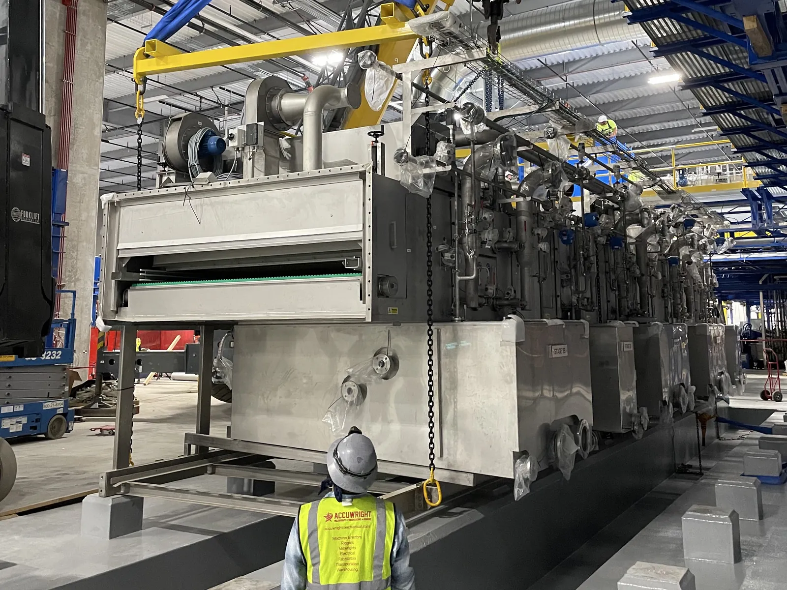 An Accuwright crew setting a long stainless process line with a spreader beam inside a bright new plant