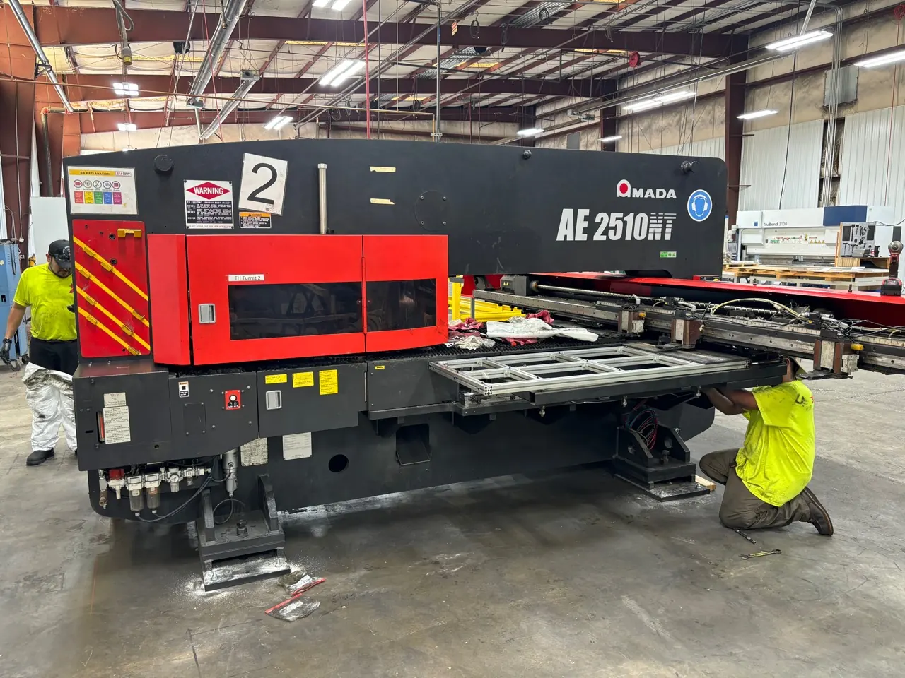 An Accuwright crew leveling and anchoring an Amada AE 2510 NT machine on a plant floor