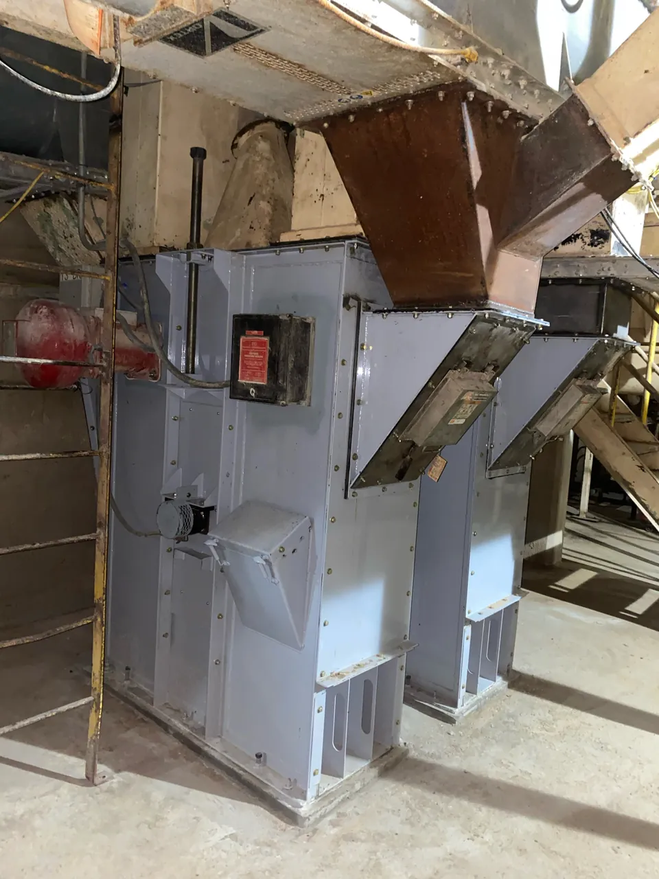 Twin gray elevator housings installed beneath existing chutes in an operating plant