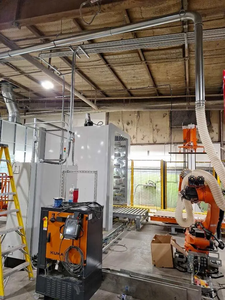 A robotic production cell with safety fencing, stainless exhaust ducting and conveyor