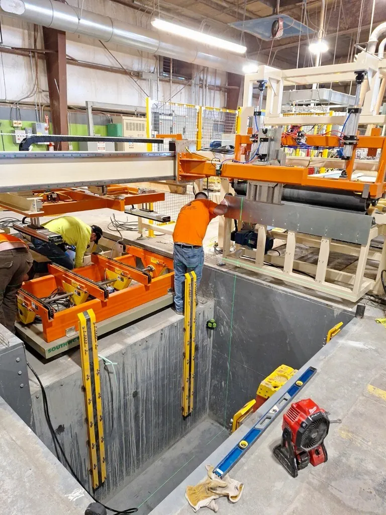 Workers installing an automated machine assembly over a deep finished equipment pit