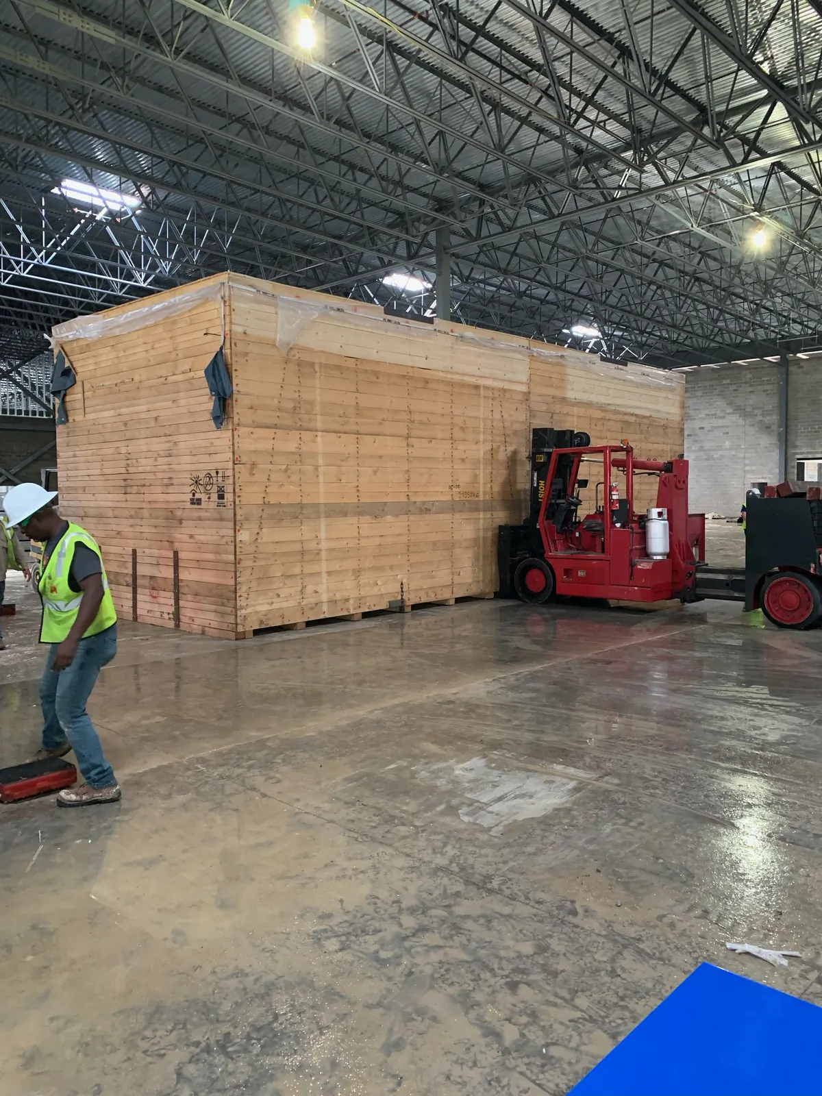 A very large wooden export crate on the warehouse floor with a red Hoist forklift alongside