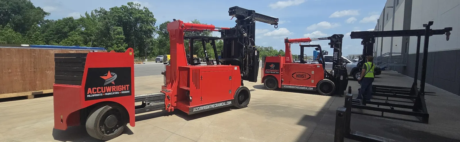 Two branded Accuwright heavy forklifts with boom attachments staged outside a plant