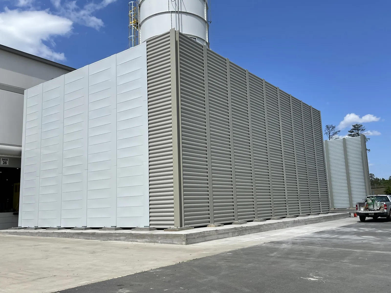 A large louvered steel screen wall installed at a plant dock beside a silo