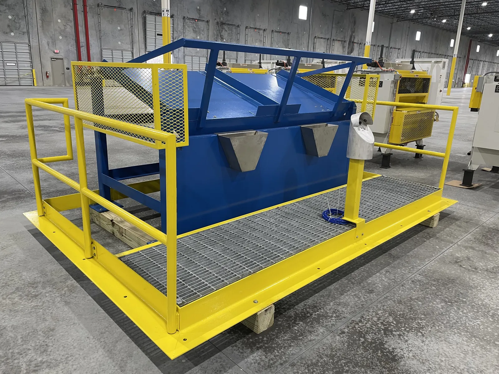 The same fabricated unit built and standing in the plant - blue frame, stainless hoppers, yellow rails and grated deck