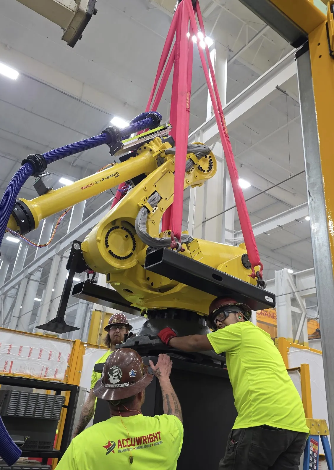 A large industrial robot suspended on round slings being guided onto its pedestal by three Accuwright crew members