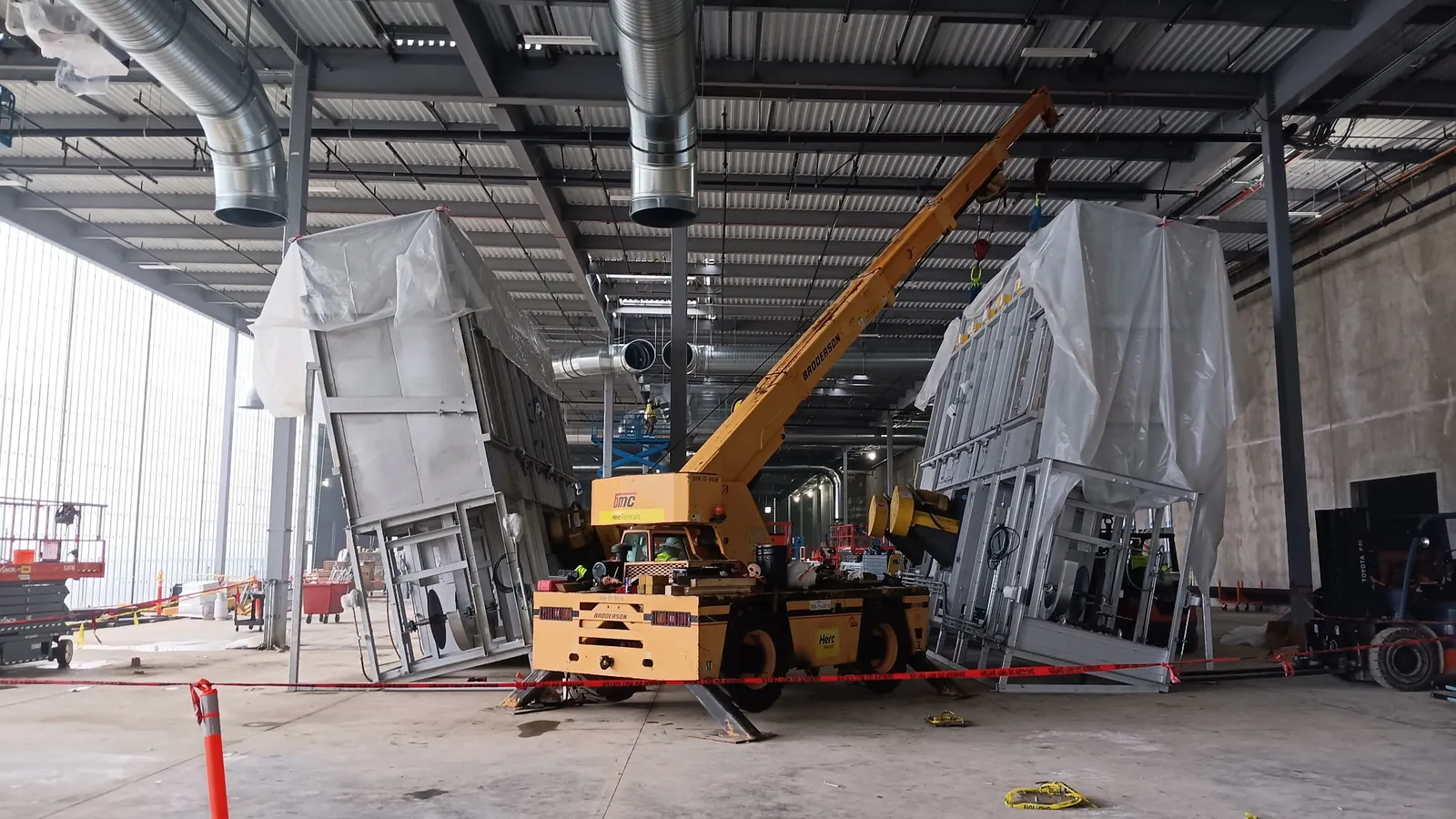 A carry-deck crane uprighting two large wrapped equipment modules inside a new plant