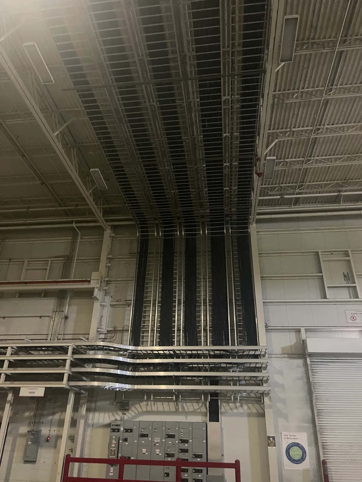Feeder bundles sweeping from wall-mounted cable tray into overhead runs above plant switchgear