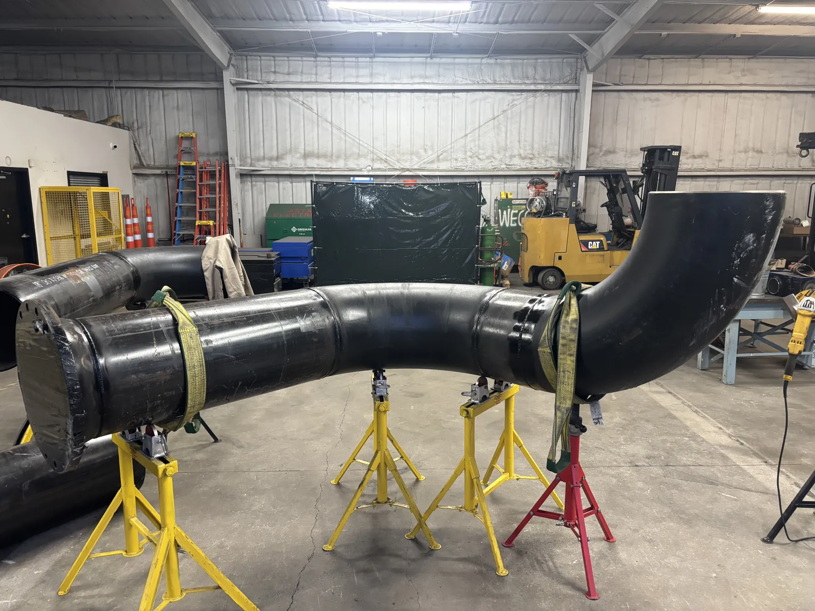 A very large diameter black pipe spool with sweeping welded elbows on pipe stands in the Accuwright shop